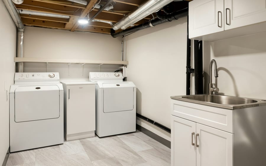 A finished basement laundry room with a utility sink under exposed joists
