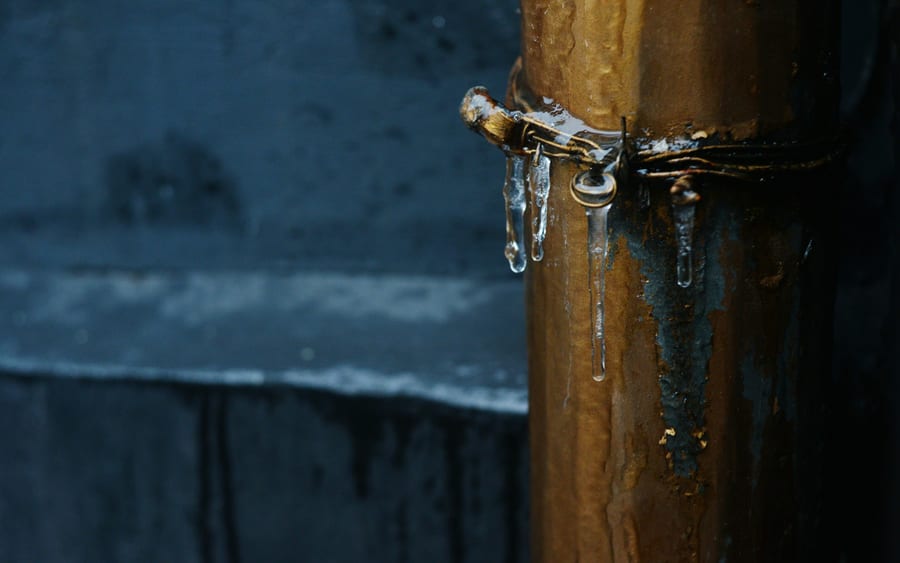 Ice hanging from a corroded metal pipe at a pipe clamp