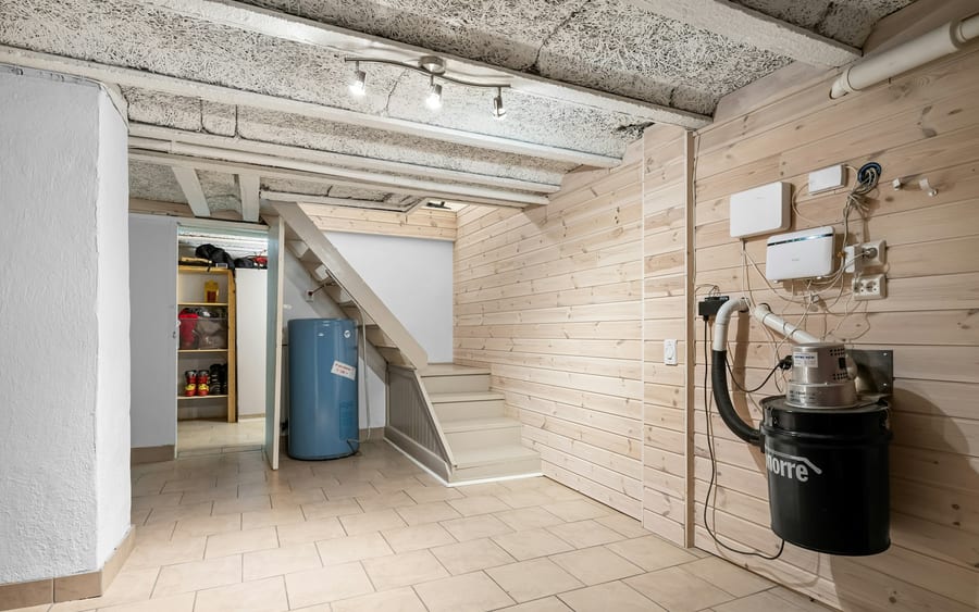 A finished basement utility room with a blue storage tank beside the stairs